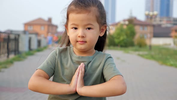 Pretty Asian Girl Holds Hands in Pray Gesture on Waterfront alt