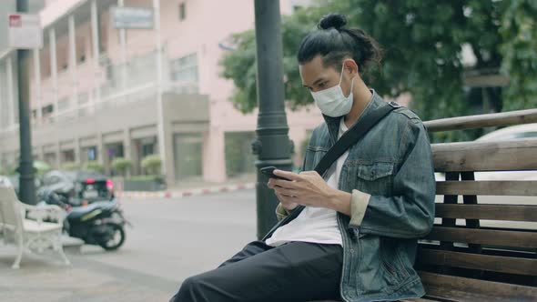 Asian man wearing a mask and using a smartphone.