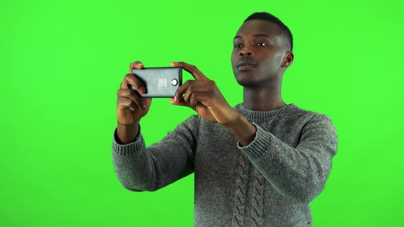 A Young Black Man Takes Pictures of Something Off the Camera with a Smartphone - Green Screen Studio alt
