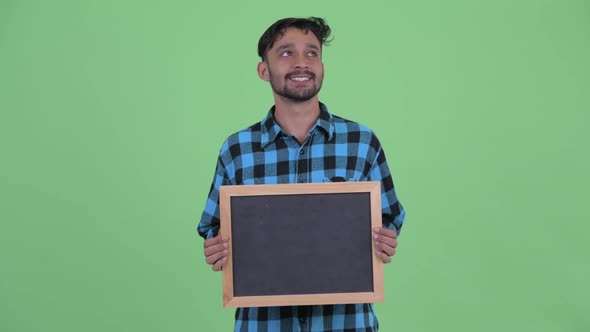 Happy Young Bearded Persian Hipster Man Thinking While Holding Blackboard alt