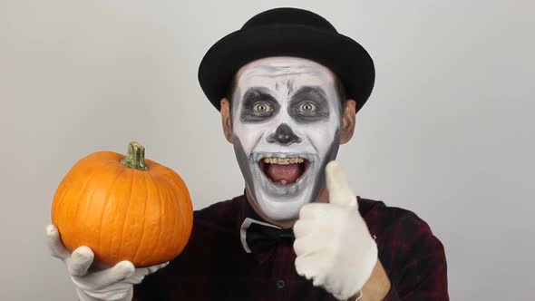 A Horrible Man in Clown Make-up Holds a Pumpkin, Symbol of Halloween. A Scary Clown Looks at the