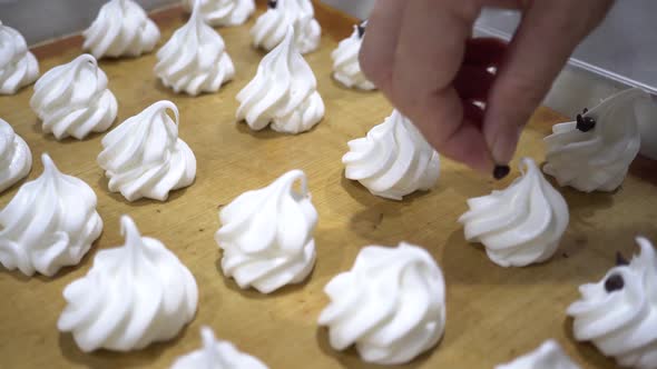 Closeup of Chef Hand Decorating White Meringues Snack with Chocolate Chip in the Kitchen Factory alt