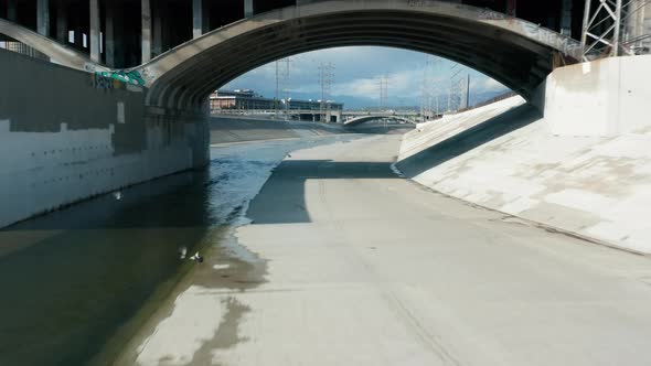 Drone Flying Under Arched Concrete Bridge Above Scenic Los Angeles River Water alt