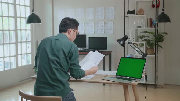 Designer Works On A Storyboard, Looks At His Sketches With Mock Up Green Screen Laptop alt