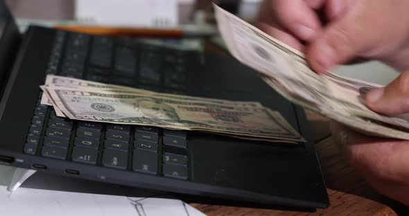Hands of Man Accountant Counting Dollar Banknotes with Writes the Result to the Note Laptop alt