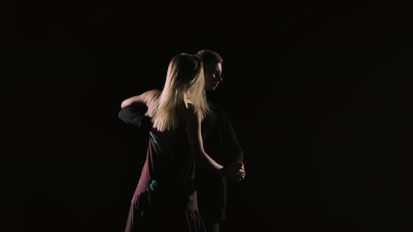 Couple of Ballroom Dancers Perform Bachata Dance Element on Black Studio Background in Darkness alt