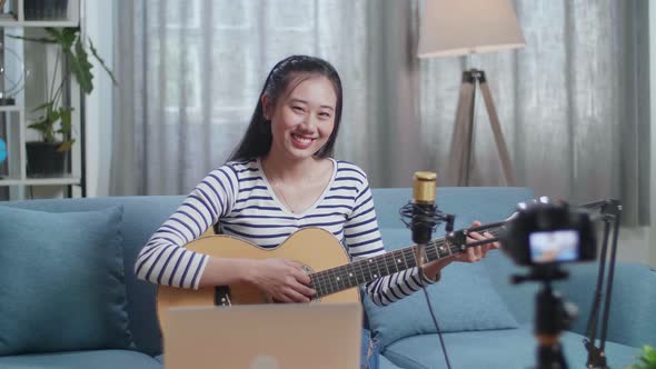 Asian Woman With A Laptop Holding A Guitar And Smiling To Camera While Live Stream At Home alt