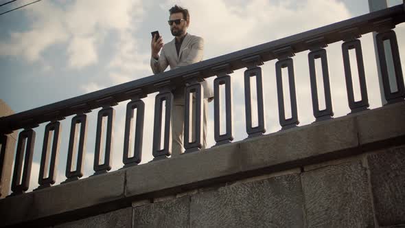 Businessman Stands On Bridge And Talking On Mobile Phone.Freelancer Cellphone Calling Online Meeting alt