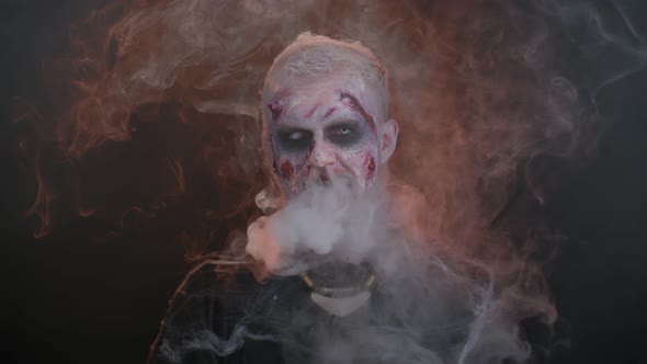 Sinister Man Horrible Scary Halloween Zombie Looking Ominous at Camera Blows Smoke From Nose Mouth alt