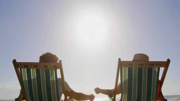 Couple relaxing on sun lounger at beach in the sunshine 