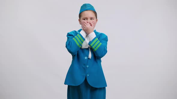 Scared Girl in Stewardess Uniform Closing Mouth with Hands Posing at White Background alt