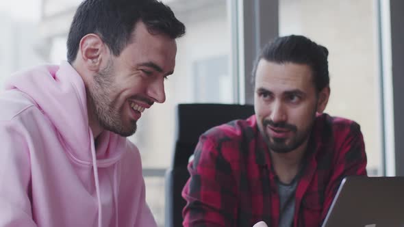 A Young Businessman with a Laptop Talks to a Colleague in the Office alt
