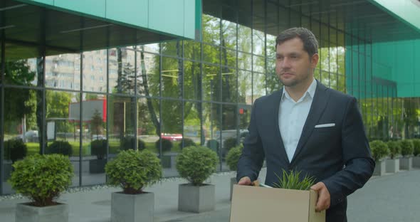 Businessman Gets Fired and Walking Near Office Center with Carton Box and Documents with a Table alt