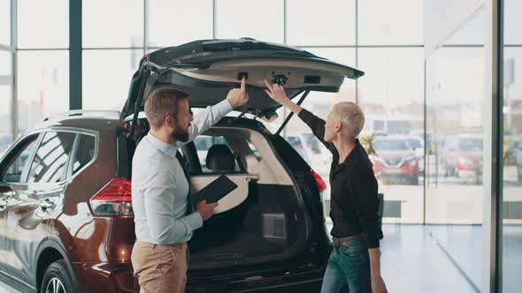 Blond Good Looking Female Customer with a Salesman Examining Car at Showroom alt
