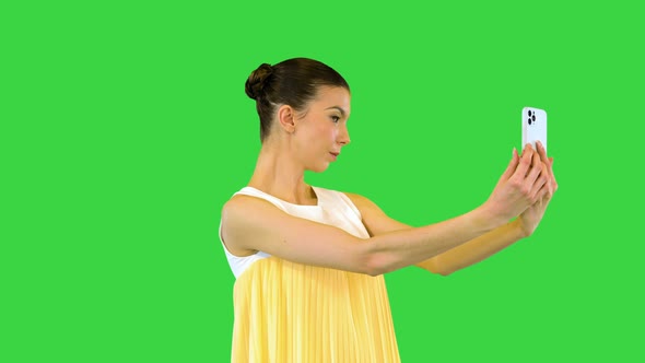 Young Beautiful Girl in Whiteyellow Dress Stands and Takes a Selfie on a Green Screen Chroma Key alt