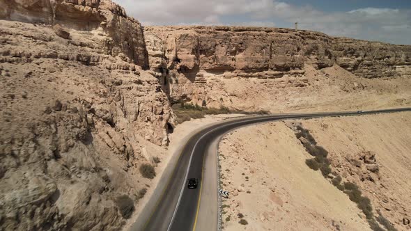 Car Driving on Asphalt Road Through the Desert Sands of the Blue Sky White Clouds