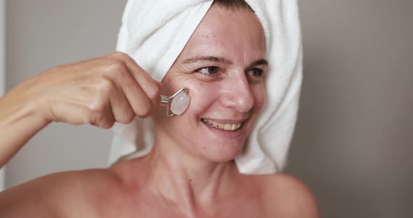 Caucasian mature woman using natural rose quartz skin care roller for her face - Beauty day concept alt