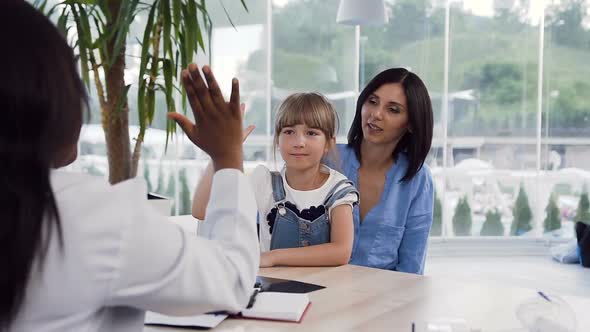 Little Girl who Sitting on the Knees of Her Mother Giving Five to Female Afican Doctor alt
