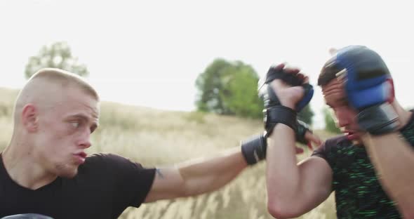 View of Two Free Fighters in Sportswear Training Kicks Among Grass on Sunset alt