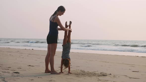 Young Sporty mother with little daughter doing gymnastic on the beach.