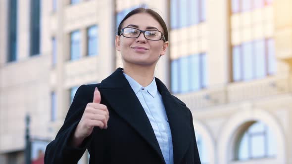 Young Confident Business Woman Shows Thumb Up Sign To Agree. Office Building on the Background alt