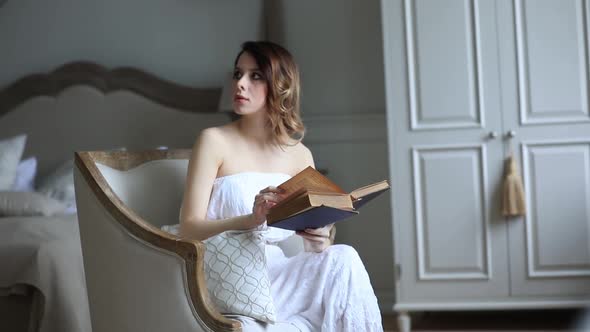 Young woman sits in armchair and reading book in vintage bedroom
