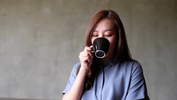 A beautiful young asian woman holding and drinking hot coffee