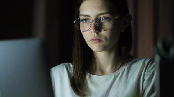 Teenage Girl with Glasses Looks at the Monitor Plays a Game Reads Studies Late at Night alt