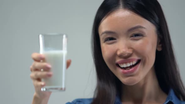 Smiling Asian Girl Showing Glass of Milk Into Camera alt