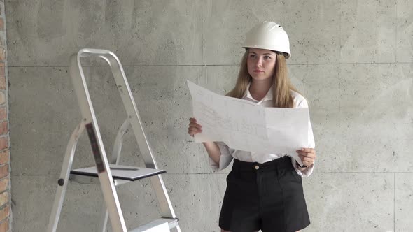 The girl engineer builder is checking the drawings at the apartment of the projected house. alt