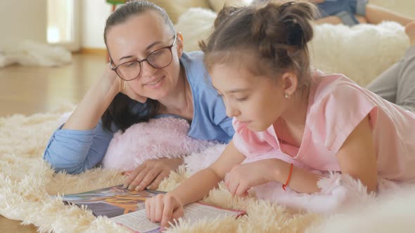 A Teenage Girl Reads a Children's Book with Her Mother Lying on the Floor in the Room alt