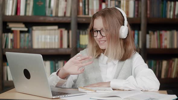 Smart Teen Girl School Pupil Wear Headphones Learning Online with Teacher Tutor Waving Hand Using alt