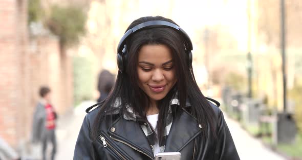 Smiling young mixed race girl listening music standing in city.
