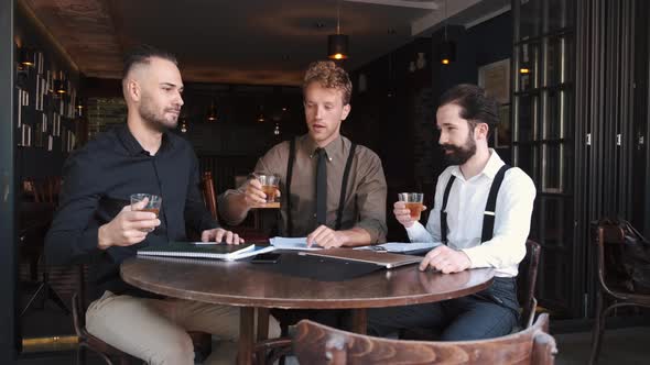 A Group of Three Stylish European Businessman Friends Entrepreneurs in a Cafe alt