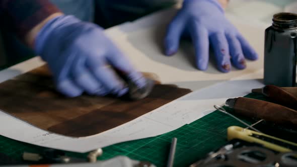 The Process of Manufacturing a Leather Wallet Handmade. The Master Paints a Piece of Leather in