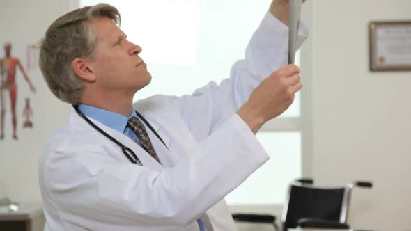 Male doctor at desk reviews x-ray alt