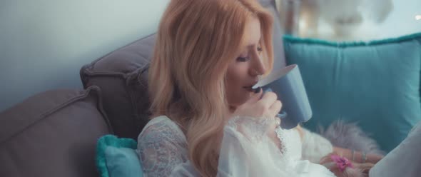 A pregnant woman drinking from a cup while enjoying a quiet time with her terrier puppies.  alt