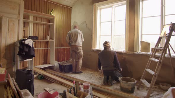 TRACKING shot R2L ZOOM OUT of 2 men plastering walls with clay, DIY alt