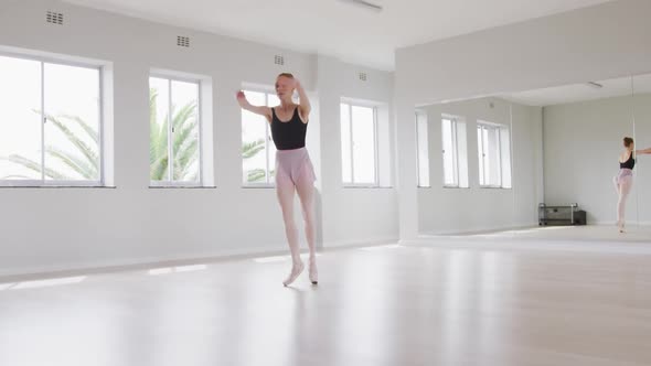 Caucasian female ballet dancer practicing ballet during a dance class in a bright studio alt