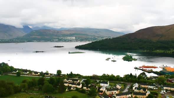 Cinematic panning drone shot of scottish lakeside village with misty mountains in background alt