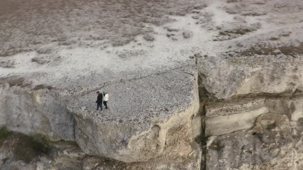 Romantic Tourist Couple Holding Hands on Cliff Edge View From Drone Above alt