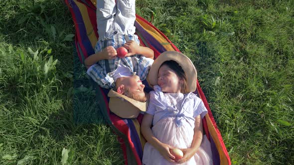 Cheerful Children in Straw Hats Are Lying on Blanket with Apples in Their Hands and Communicate at alt
