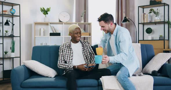 Homosexual with Cups of Freshly Brewed Beverage Approaching to His African American Boyfriend alt