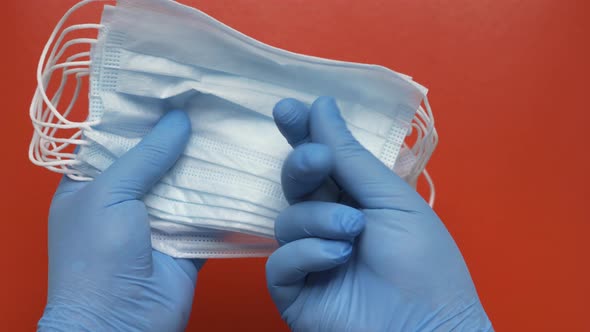 Doctor Showing Medical Face Mask Holding in Hands Blue Gloves on Red Background, Shows Fingers