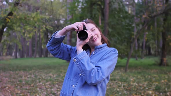 Cute Hipster Photographer Girl Takes a Picture on a Professional Camera and Smiles