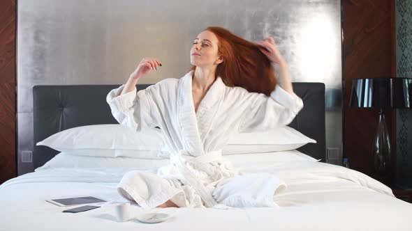 Redhead Girl in White Bathrobe on Bed in Hotel Room