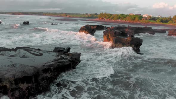 A Beautiful Bird'seye View of Flying Around the Black Rocks on Ocean at the Golden Hour alt