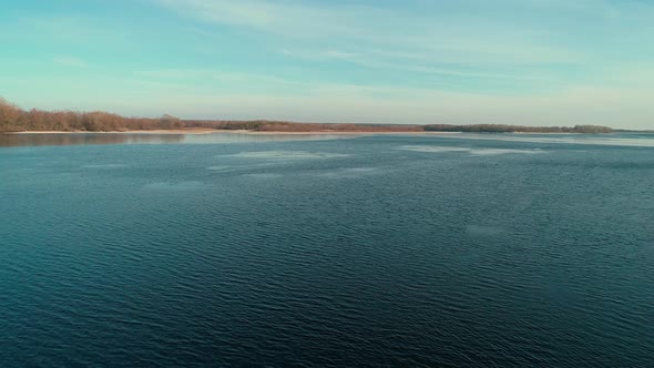 Aerial Drone Footag of Flying Over a Calm River in Winter Forest in the Distance