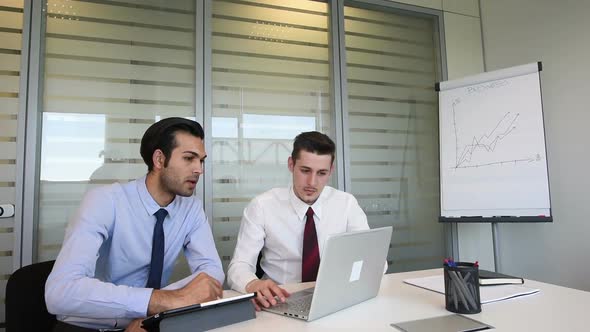 two young business man indoor office interior using personal computer and digital tablet, discussing alt