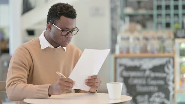 African American Man Reading Documents While Drinking Coffee in Cafe alt